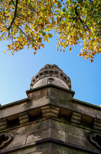 A view of Severndroog Castle garden showing well-maintained flower beds with lush green foliage, including flowering shrubs and small trees, situated in front of a historic red-brick building with dis